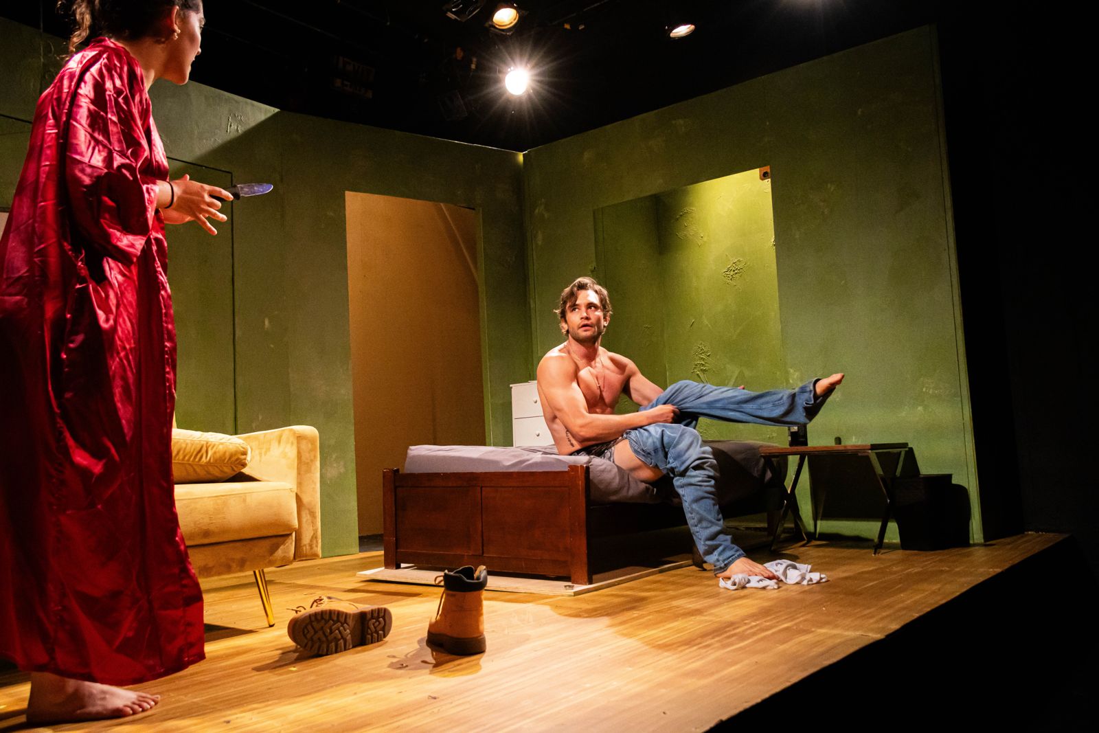 The Motherfucker with the Hat: a woman in a red robe faces a shirtless man on a couch